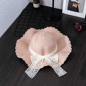 Detail of summer straw sun hat featuring a large lace bow and elegant wavy brim