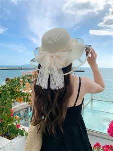 Close-up of beige woven straw hat with large lace bow and pearl accents for summer