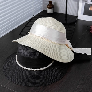 Detail of hand-woven straw hats featuring elegant satin bows and pearl string decorations