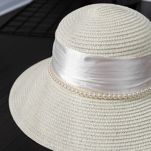 Close-up of woven straw hat featuring elegant white satin ribbon and pearl trim detail