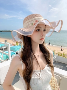Detail of beige straw sun hat with white mesh edge and green floral embroidery