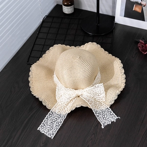 Summer straw sun hat with large lace bow and wavy brim for women on a table