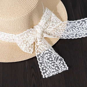 Close-up of woven boater hat featuring elegant white floral lace ribbon and bow details