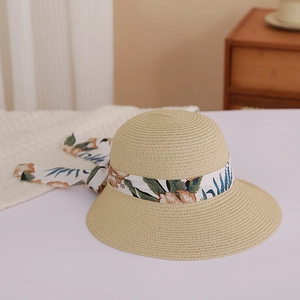 Detail of wide brim straw hat with floral ribbon bow on a minimal white surface