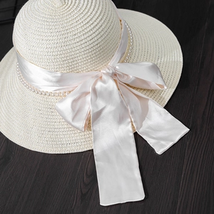 Close-up of elegant straw hat with pink satin bow and white pearl band detail