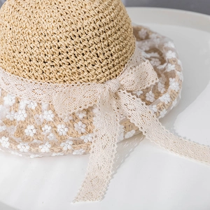 Detailed view of wide straw sun hat with delicate white lace bow and floral embroidery