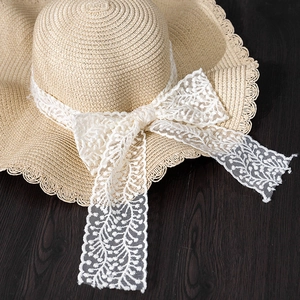 Close-up of beige woven straw hat with white embroidered lace ribbon and elegant bow