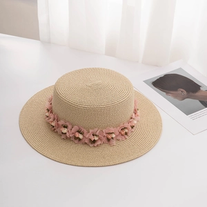 Women's summer straw hat with sweet pink floral trim on a white decorative table