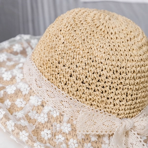 Close-up of beige straw sun hat with white daisy floral lace and delicate bow detailing