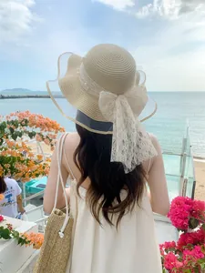 Detail of straw sun hat with large white lace bow and pearls on wavy brim back view