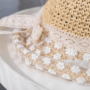 Detailed close-up of straw sun hat featuring elegant white lace and daisy floral embroidery