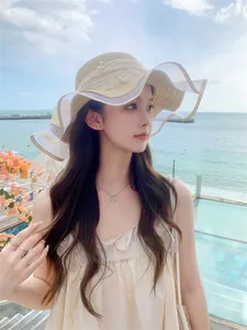 Close-up of beige straw sun hat featuring wavy lace brim and delicate pearl accents