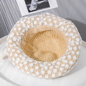 Detailed macro view of woven straw hat featuring floral lace embroidery and delicate ribbons