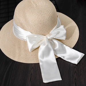Detailed close-up of straw hat featuring a wide white ribbon bow and pearl bead accents