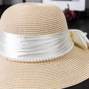 Detail of elegant straw hat featuring white satin bow and delicate pearl embellishments