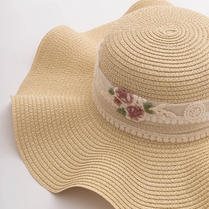 Close-up of beige straw hat featuring delicate lace ribbon and floral embroidery details