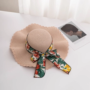 Detail of woven straw sun hat featuring wavy scalloped brim and floral silk ribbon bow