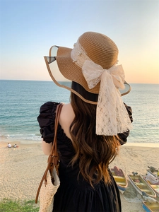 Detailed view of women's straw sun hat with lace bow, pearls, and wavy brim for beach vacations