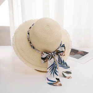 Beige wide brim straw sun hat with tropical print ribbon and pearls on a white table