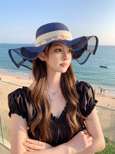 Detail of navy straw sun hat with white lace trim and pink floral accent on wide brim