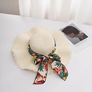 Detail of wide-brim straw hat featuring wavy scalloped edges and floral ribbon bow