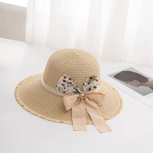 Close-up of wide-brim straw hat featuring fringe edges and a large floral bow with pearl buckle