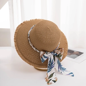 Detail of a brown woven straw sun hat featuring a fringed brim and floral ribbon with pearl