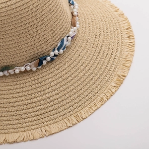 Detailed close-up of straw sun hat with fringe edge, pearls and patterned silk ribbon