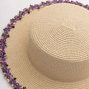 Macro shot of straw sun hat with detailed purple flower embroidery on the brim