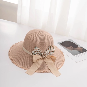 Detail of a beige straw hat featuring a floral bow and sparkling rhinestone buckle