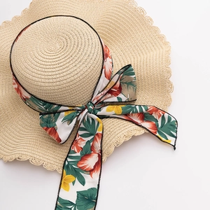 Close-up of wavy brim edges and floral ribbon bow on a woven straw beach hat