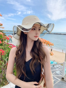 Close-up of beige straw sun hat with pearl accents and wavy black lace brim on a beach
