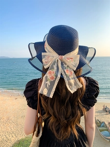 Close-up of a giant beige lace bow with floral embroidery on a navy blue straw sun hat