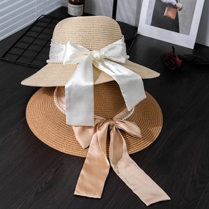 Detail of woven straw sun hats with elegant satin bows and decorative pearl chains
