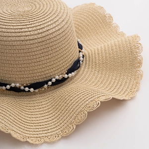 Detail of beige straw hat featuring scalloped wide brim with pearl and rhinestone band