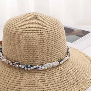 Detail of wide brim straw hat featuring pearl ribbon trim and frayed edge texture