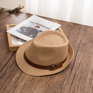 Detail of light brown straw fedora with dark leather band and metal buckle on wood