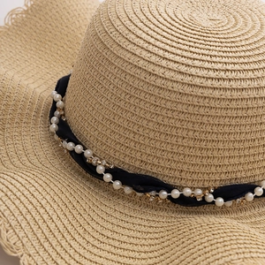 Close-up of straw sun hat featuring a black ribbon with pearls and rhinestone details