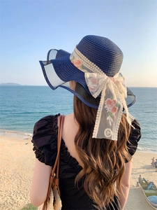 Detail of navy blue straw sun hat with white lace ribbon and flower embroidery at the beach