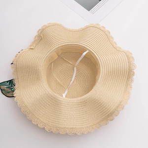 Detail view of wavy lace brim and decorative green leaf bow on the straw beach hat