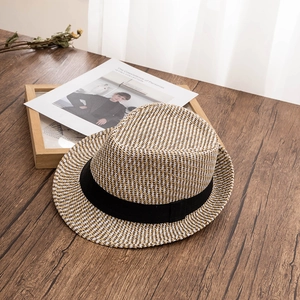 Detail view of woven straw fedora texture and black ribbon band on wooden surface