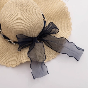 Detailed close-up of wide brim straw sun hat featuring pearl beads and a navy mesh bow