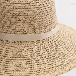 Close-up of woven straw sun hat featuring beige ribbon and fringed tassel edge details