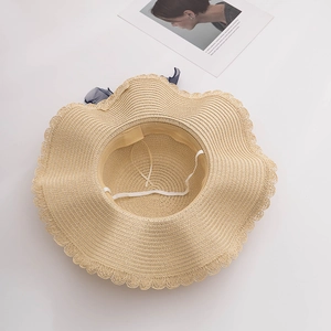 Detail of wide brim straw hat featuring wavy edges and elegant navy blue chiffon ribbon