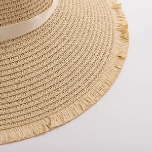 Close-up of woven straw sun hat edge with cream ribbon and delicate fringe detail
