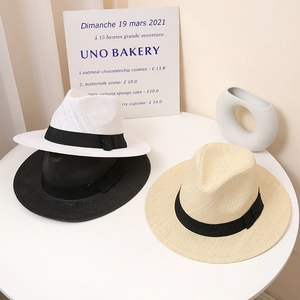 Three wide brim straw sun hats in white, black and beige on table with elegant ribbon