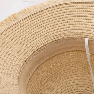 Detail of straw sun hat featuring woven texture, frayed brim, and interior sweatband