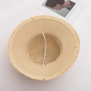Close-up of a straw sun hat with frayed tassel edges and a white elastic chin strap