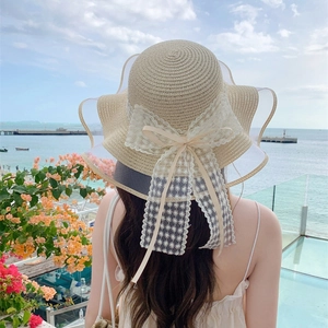 Cappello da sole in paglia beige da donna con grande fiocco in pizzo e bordo ondulato
