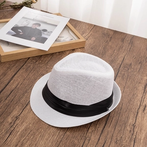 Detailed weave of a white straw fedora with black satin ribbon on dark wood surface